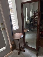 Wooden cheval mirror and hexagon side table positioned near a door, showing full length of mirror and table shape.