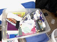 Clear bin filled with assorted fabric remnants, including folded pieces and bags containing smaller scraps, along with some supplies like a plastic case with a floral design.