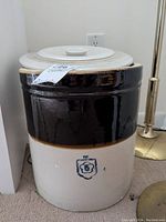 Front view of the farmhouse crock showing the two-tone brown and cream coloring and the blue emblem on the front.