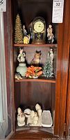 Photo of cabinet shelves showing clock, figurines including owl and human shapes, porcelain flower, ceramic roosters.
