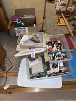 Overview photo showing bins with assorted sewing and crafting supplies including thread spools, a white hem marker tool, fabric pieces, and craft kits.