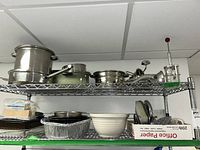 Two shelves showing pots, pans, bowls, disposable aluminum pans, white mixing bowl, paper office paper box, and assorted kitchen containers.