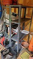 Two metal shelving units standing side by side inside a wooden shed with gardening and storage items around them.