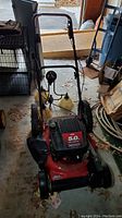 Overall view of the red gas powered mulching lawn mower showing the handle, wheels and usual lawn mower structure.