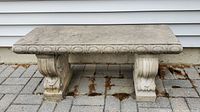 Front-facing photo of rectangular outdoor cement bench with decorative legs showing weathered surface.