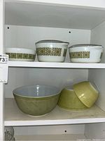 Shelf with 3 glass Pyrex baking dishes with green geometric patterned borders and 3 green mixing bowls below.