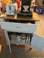 Front view of rolling kitchen cabinet with drawer partially open and double-door cabinet open below, showing some kitchen items inside (not included).