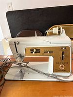 White Singer Golden Touch & Sew Deluxe Zig-Zag model 620 sewing machine sitting on wood table. Machine has gold control panel with knobs and stitches settings.