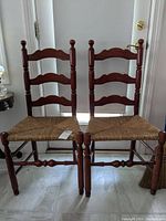 Front view of two vintage ladderback chairs side-by-side, showing woven seats and turned wood legs.