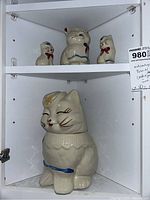 Photo of the full set inside a white cabinet, showing the large Puss N Boots cookie jar at bottom and the smaller salt and pepper shakers and cream pitcher on the upper shelf.