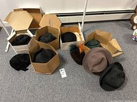 Overview of eight vintage women's hats arranged on the floor, with some placed in vintage cardboard hat boxes of hexagonal and rectangular shapes.