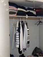 Closet view showing hanging blouses and shirts, and folded clothing on shelf above