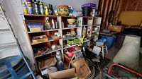 Wide view of wooden shelving with assorted garden and home supplies including planters, bottles of liquids, pest control sprays, and garden tools