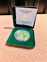 Front image of silver coin in green velvet display box with certificate card showing maple leaf design and coloured enamel details.