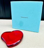 Heart-shaped red crystal paperweight positioned beside Tiffany & Co. blue box showing brand logo on box lid.