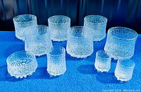 Set of 11 Iittala Ultima Thule glassware pieces arranged on blue cloth, showing textured surface and varied sizes.
