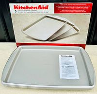 Three KitchenAid cookie pans stacked with packaging in background showing original box and instructions inside tray.