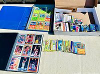 Wide view showing blue binder filled with Pokemon cards, black binder with basketball cards, and box with mixed sports cards and packs