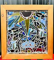 Full view of signed slag glass mosaic window panel in wooden frame showing colorful abstract geometric pattern.