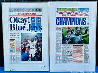 Two framed posters displayed side by side. Left poster titled 'Okay! Blue Jays', signed by Joe Carter in bottom right corner. Right poster titled 'Champions' showing celebration during World Series win.