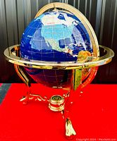 Full front view of globe mounted on gold-tone tripod stand, showing lapis lazuli oceans and multi-stone continents
