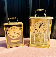 Both brass mantle clocks shown side by side on a pink surface with a black background.