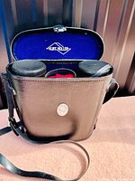 Binoculars inside the black carrying case with blue Karl Muller lining visible.