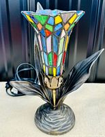 Full view of lamp showing tulip-shaped slag glass shade with multicolored stained glass pieces and dark metal leafy stem and base.