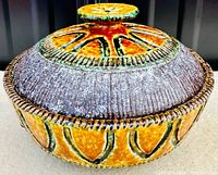 Top view of the lidded casserole showing intricate orange and green festive pattern on the lid with textured brown rim.