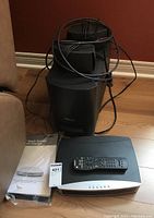 View of Bose AV3 II media center, remote control on top, two small bookshelf speakers, cabling, and user manual on the floor next to units.