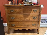 Front view of oak dresser showing three drawers with ornate brass handles, visible wood grain, and scalloped apron at base.