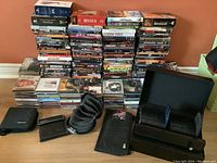 Wide view showing stacks of DVDs and music CDs including Elvis collections, with multiple storage cases in front on hardwood floor against orange wall.