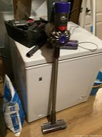 Full view of Dyson V8 Animal cordless vacuum with metal wand, motorized floor head, and accessories in background.