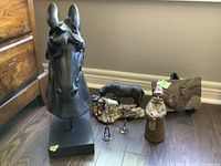 View of all items in the lot: composite horse head sculpture, two wire horse figures, ceramic gnome, hand-casted horses at well, wooden carved horse panel.
