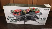 Box of Cuisine Essentials Hot Stone Grill featuring image of grill with vegetables and product listing on front.