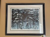 Framed print showing snow-covered evergreen trees in a winter forest setting, behind glass.