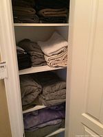 Photo of three shelves loaded with neatly folded assorted towels and blankets in beige, brown, and cream tones inside a linen closet.
