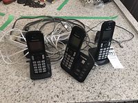 Three black Panasonic cordless phones with charging bases viewed from front angle, showing keypads and screens.