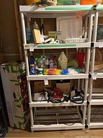 Front view of white resin storage shelf with various contents displayed, including cleaning supplies and household items. Shelf dimensions approximately 36x18x73 inches, multi-tiered construction with vented shelves.