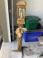 Full view of rustic wooden outdoor patio light showing the wooden post, glass bulb holder and decorative dried plants attached to post.