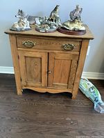 Front view of the vintage solid wood table showing the drawer and cabinet doors, with various animal figurines positioned on top.