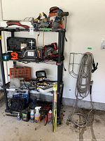Full view of metal shelving unit with tools displayed on shelves and hose hung on adjacent wall rack.