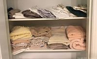 Photo of folded bath towels and linens stacked on shelves with colors yellow, beige, brown, peach, green, and grey.