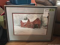Framed limited edition print of a red barn in winter setting with snow and trees. Shows the entire framed artwork with label on upper right corner.