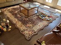 Full view of the brown floral wool area rug with scalloped edges, showing general condition and placement in a living room with furniture.