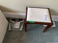 Weight Watchers digital bathroom scale placed near the wooden stool on a blue tile floor with user manual on top of it.