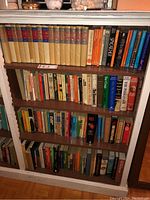 Full shelving unit with multiple shelves filled with assorted books including a visible collection of hardcover novels with dust jackets and other varied books