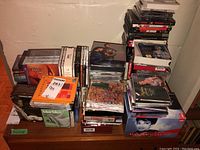 Wide view of multiple stacks of CDs on floor against wall showing classical and opera music collections, including boxed sets.