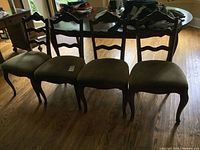 Four matching solid wood dining chairs with ladder-back design and wide upholstered seats in neutral geometric patterned fabric, arranged side by side on a wood floor