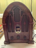 Front view of the General Electric wood panel reproduction radio showing the arched top, carved column details, patterned speaker grill, central dial and three control knobs at the base